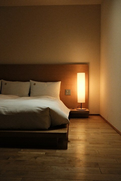 Minimalist bedroom with wooden bed, white linens, and warm lamp